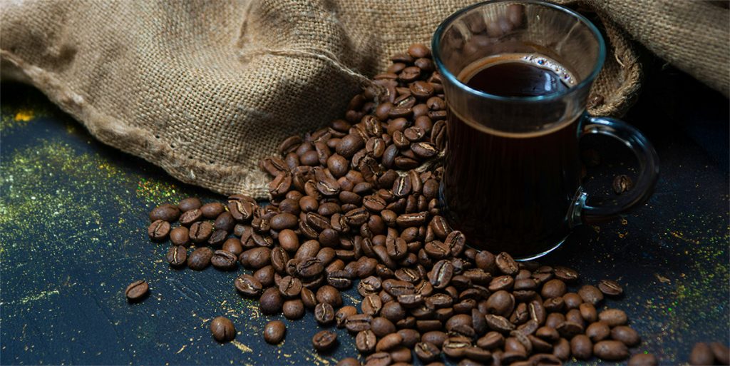 An enticing cup of coffee next to a bag of roasted coffee beans spilling out in abundance.